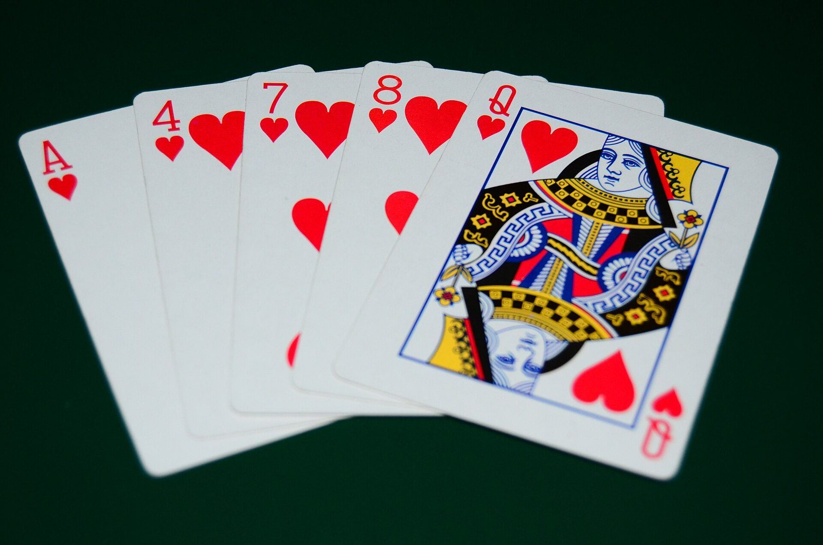 Cinco cartas de corazones abiertas en abanico sobre paño verde oscuro: as, 4, 7, 8 y reina, un color sin secuencia