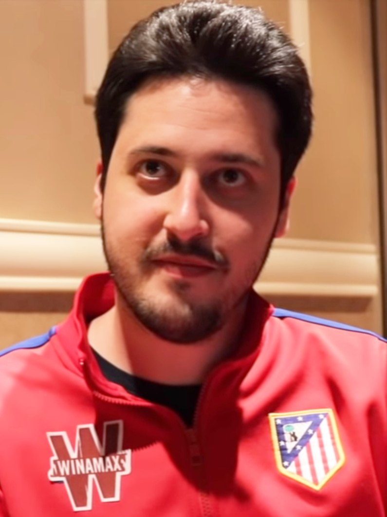 Retrato de Adrián Mateos, de barba corta y pelo oscuro, con una chaqueta roja con el escudo del Atlético de Madrid, durante una entrevista